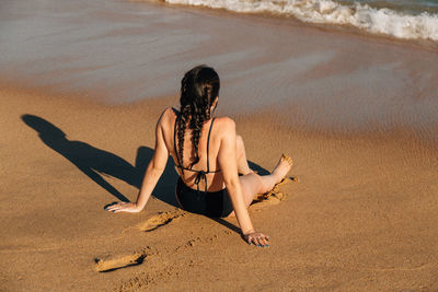 Rear view of woman sitting on sand at beach