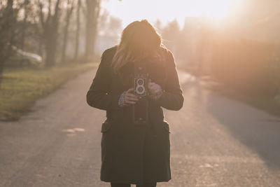 Young woman photographing through camera on road