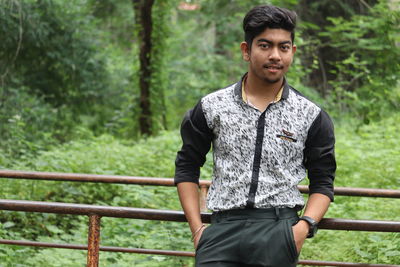 Portrait of young man standing against railing at park