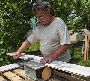 Caucasian senior man using circular saw for cutting parquet plank in the garden