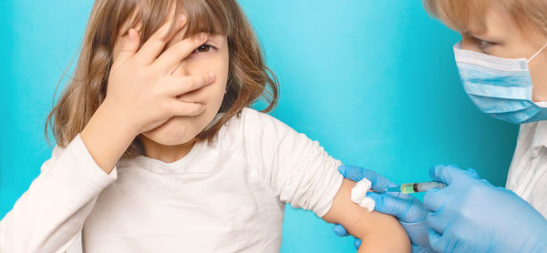 Doctor giving vaccination to girl against blue background