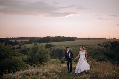 Full length of newlywed couple walking on grassy field