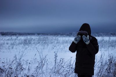 Person wearing warm clothing standing on field against sky during winter