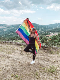 Woman standing with rainbow flag against sky