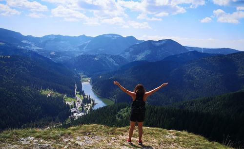 Rear view of woman with arms raised against mountains