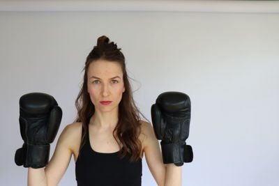 Portrait of young woman holding camera against wall