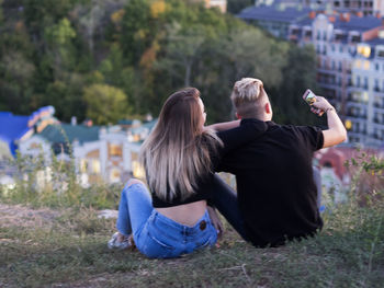 Rear view of couple taking selfie while sitting on hill