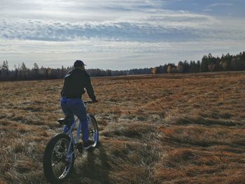 Rear view of man riding bicycle on field