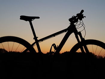 Silhouette of bicycle on field against sky at sunset