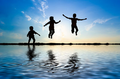 Silhouette men jumping in water against sky