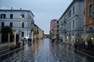 People walking on wet street amidst buildings in city