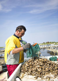 Man removing oysters in from net while working against sky