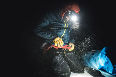 Male alpine climber putting on a jacket in the dark with blowing snow