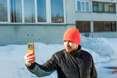 Man in warm clothing taking selfie through mobile phone