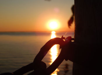 Close-up of silhouette hand against sea during sunset