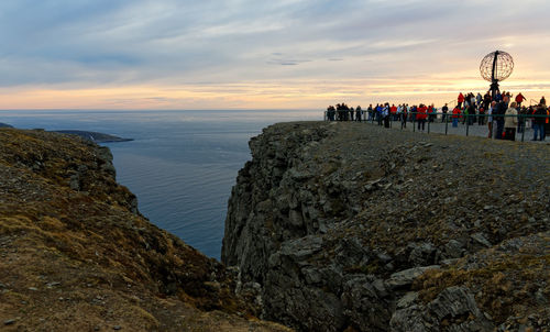 Group of people on rock by sea against sky