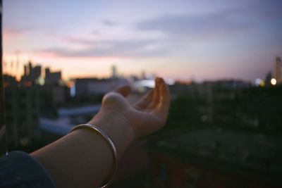 Close-up of hand holding cityscape against sky during sunset