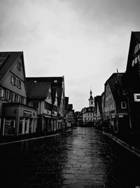 Wet street amidst buildings against sky