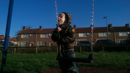 Boy holding swing with mouth open in yard