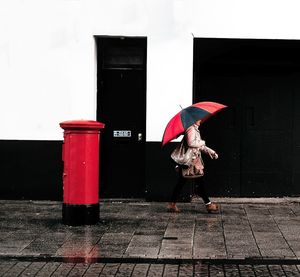 Woman with umbrella walking on sidewalk during rainy season
