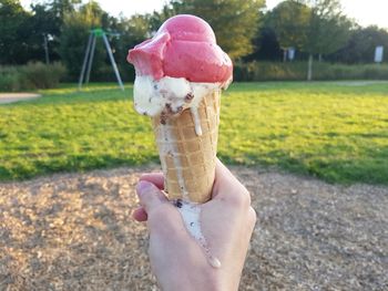 Close-up of hand holding melting ice cream in park