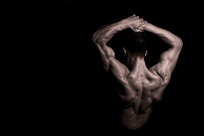 Rear view of shirtless body builder with arms raised against black background