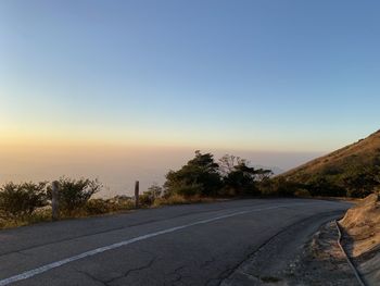 Road by trees against sky during sunset