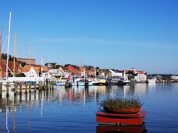 Sailboats moored in river by buildings against blue sky