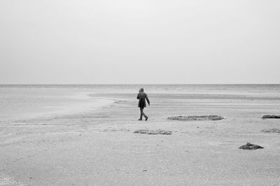 Rear view of woman walking at beach against clear sky