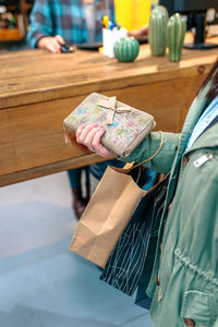 Unrecognizable woman client holding wallet with bow and ecological shopping paper bags on store