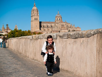 Portrait cute siblings standing on road against historic building