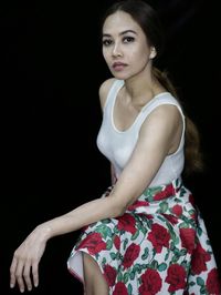 Portrait of young woman standing against black background