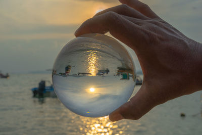 Close-up of hand holding crystal ball against sea