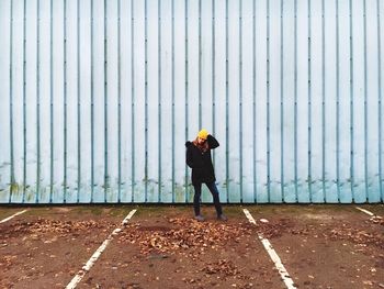 Woman standing by dry leaves fallen at parking lot against corrugated fence