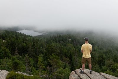 Rear view of man standing on mountain against sky