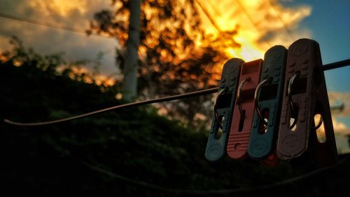 Close-up of clothespins hanging on rope against sky during sunset