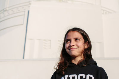 Twelve year old girl wearing a hoodie smiles while looking away