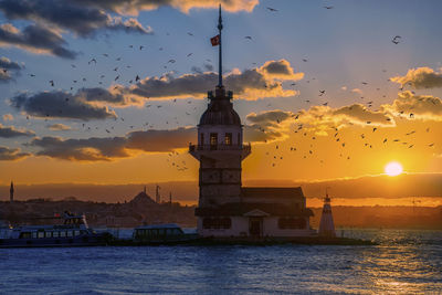 Lighthouse by sea against sky during sunset