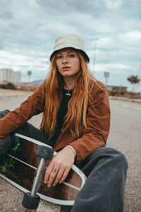 Young woman wearing hat sitting on seat against sky