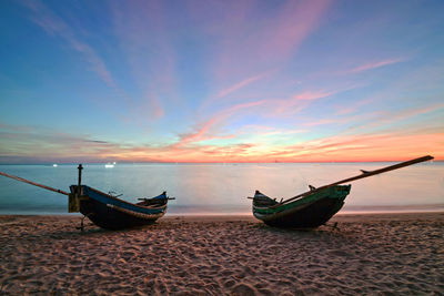 Boat moored on shore against sky during sunset