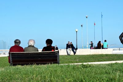 People sitting on field against clear sky