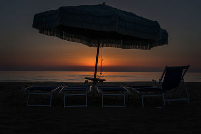 Deck chairs on beach against sky during sunset