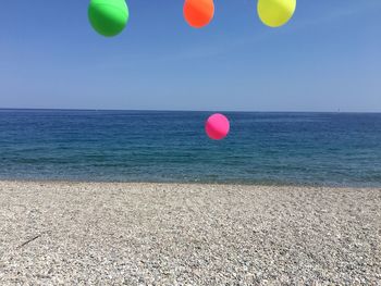 Multi colored balloons on beach against blue sky