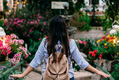 Rear view of woman wearing backpack against flowering plants