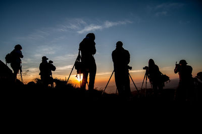 Silhouette people photographing with camera against sky during sunset