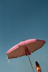 Woman standing under parasol against clear blue sky
