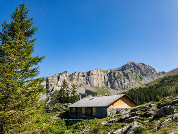 House amidst trees and mountains against clear blue sky
