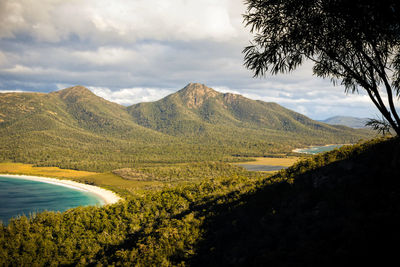 Scenic view of mountains by beach against cloudy sky