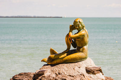 Statue on rock at beach against sky