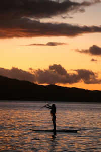 Silhouette man fishing in sea against sky during sunset